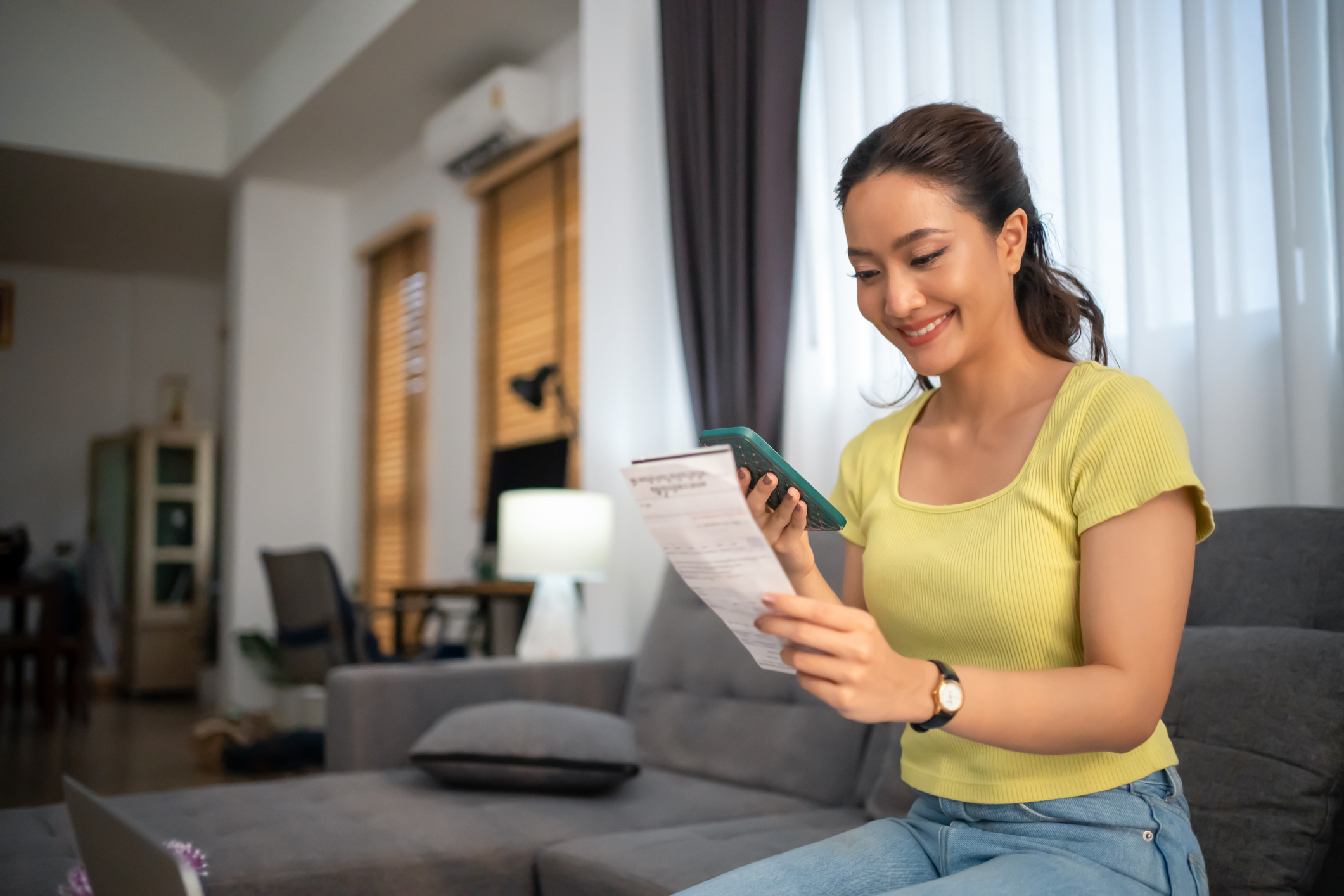A woman sitting on the sofa with a mobile phone paying bills at home