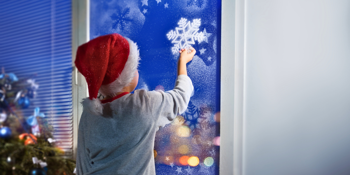 Child hanging snowflake decoration to window