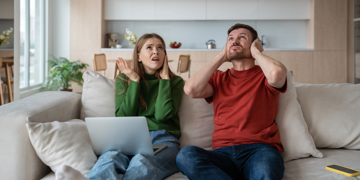 A couple covering their ears from the noise in their living room.