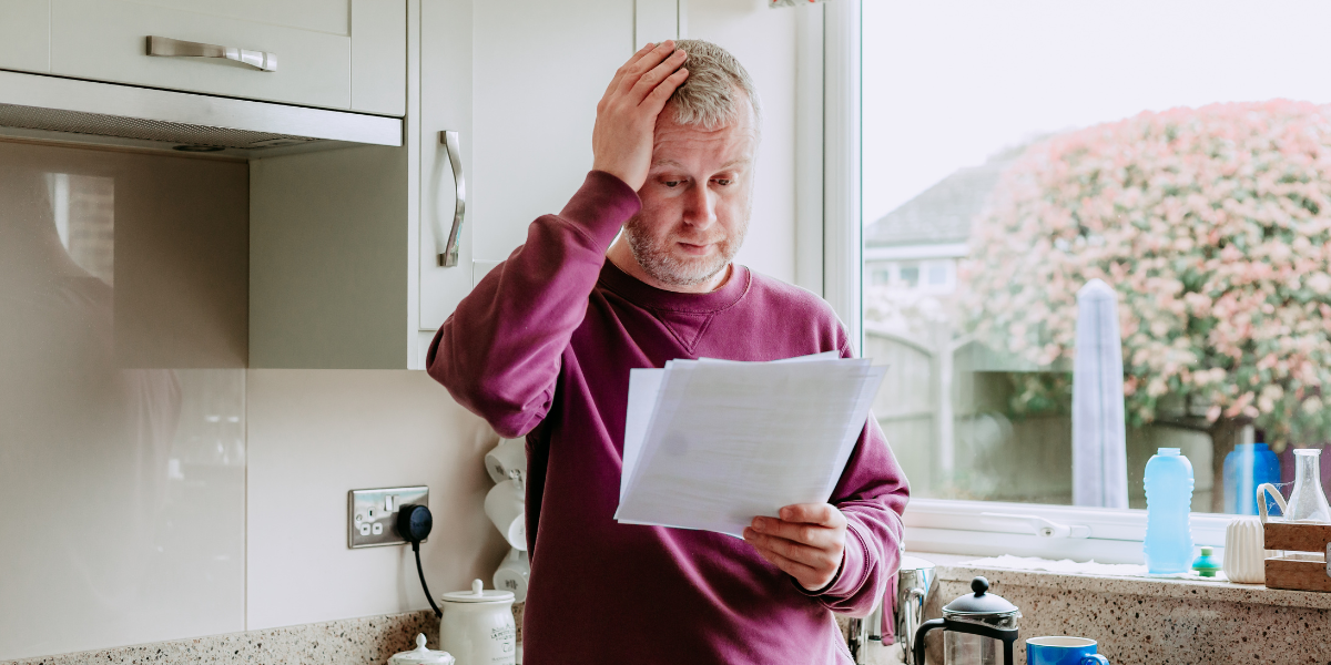 Man holding his hand to his head while reading an electric bill in his kitchen,