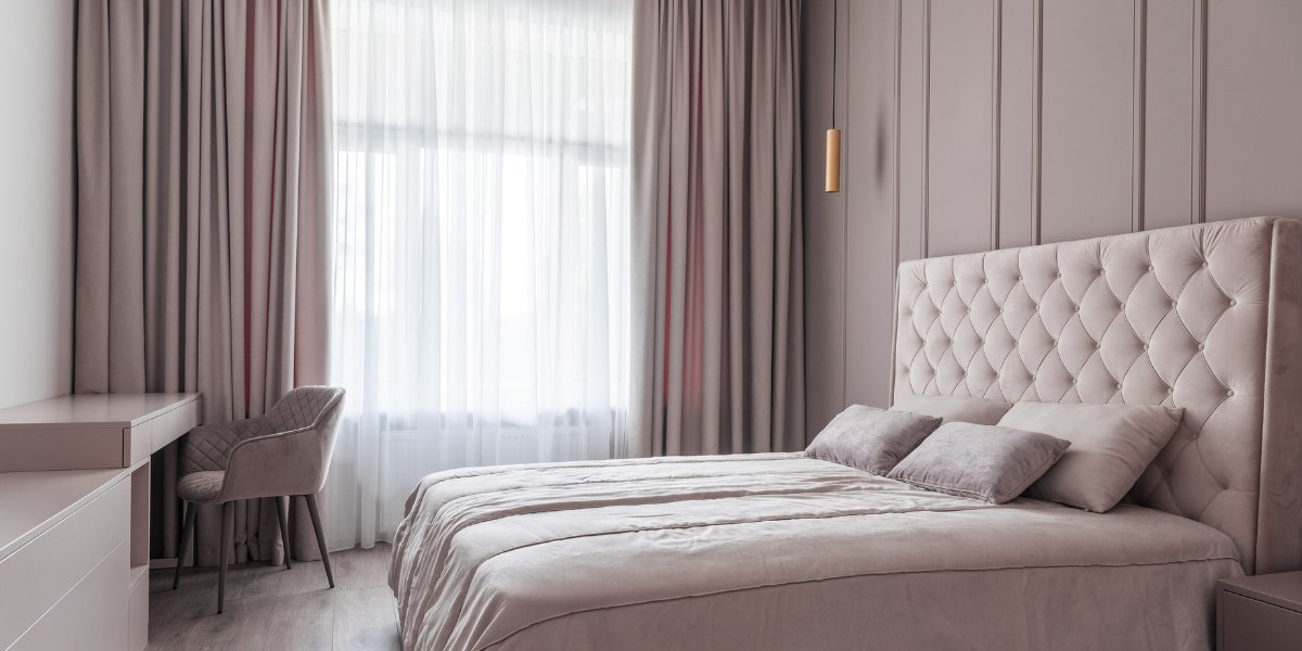 Thick velvet curtains over sheer linen curtains hang over a large bedroom window.