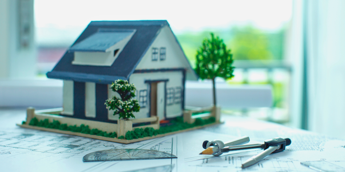 A model of a house on a drafting table with blueprints.
